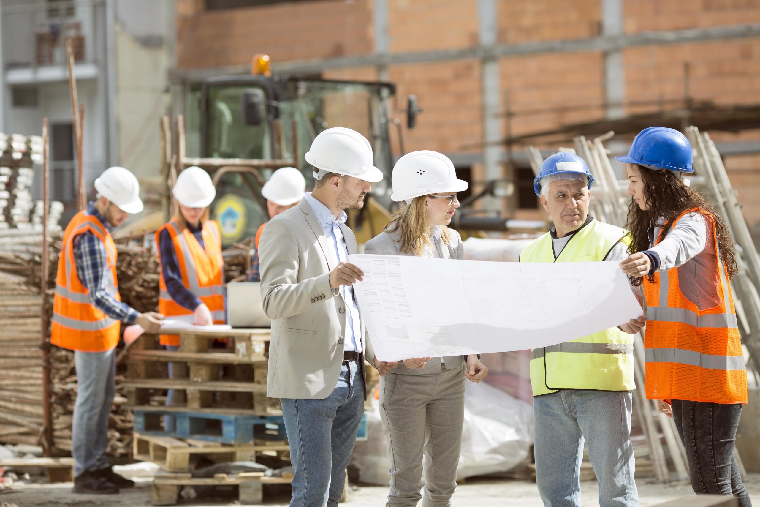 Four construction workers holding and discussing blueprints at a job site
