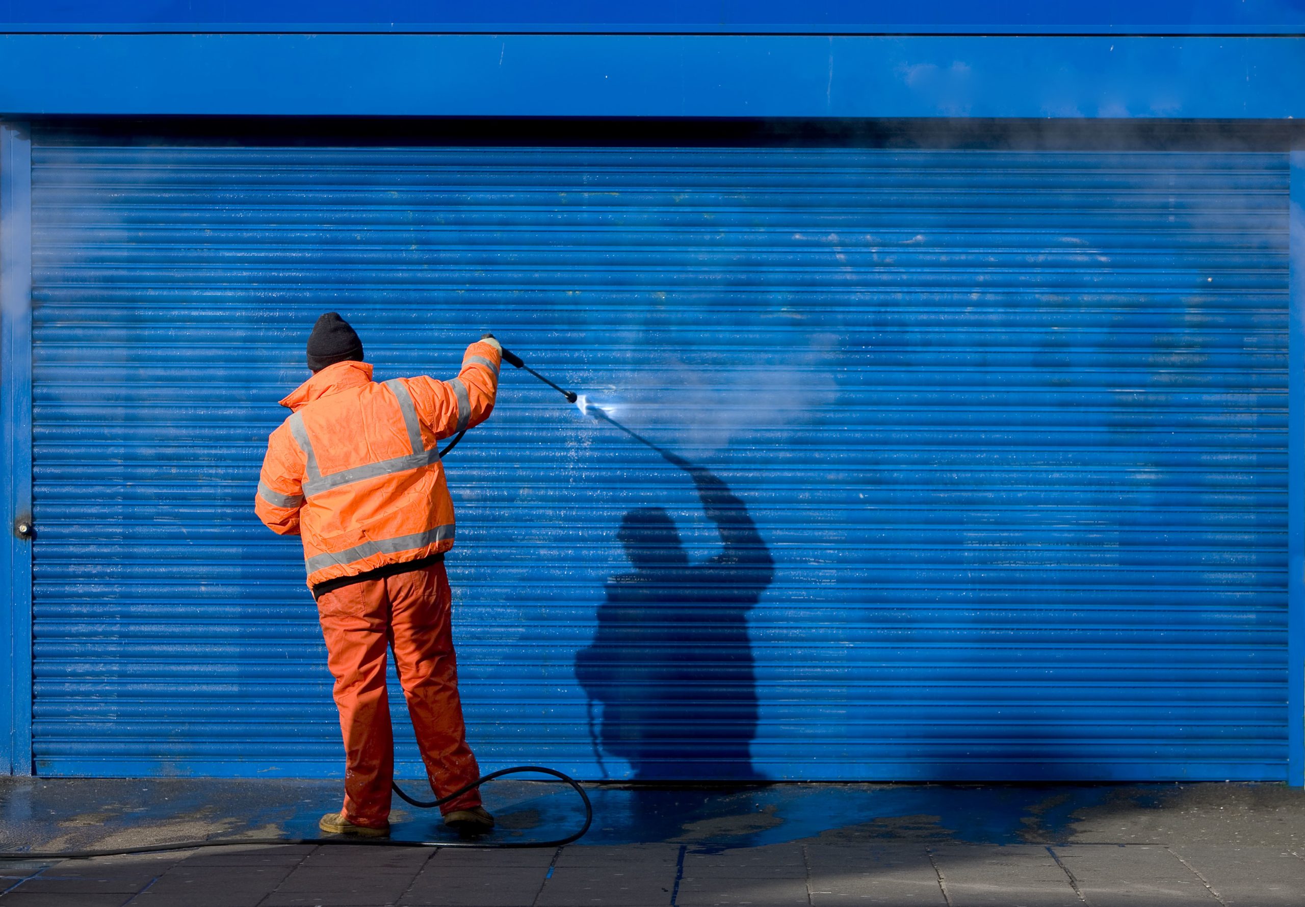 Man in orange suit removing graffiti from a blue garage door