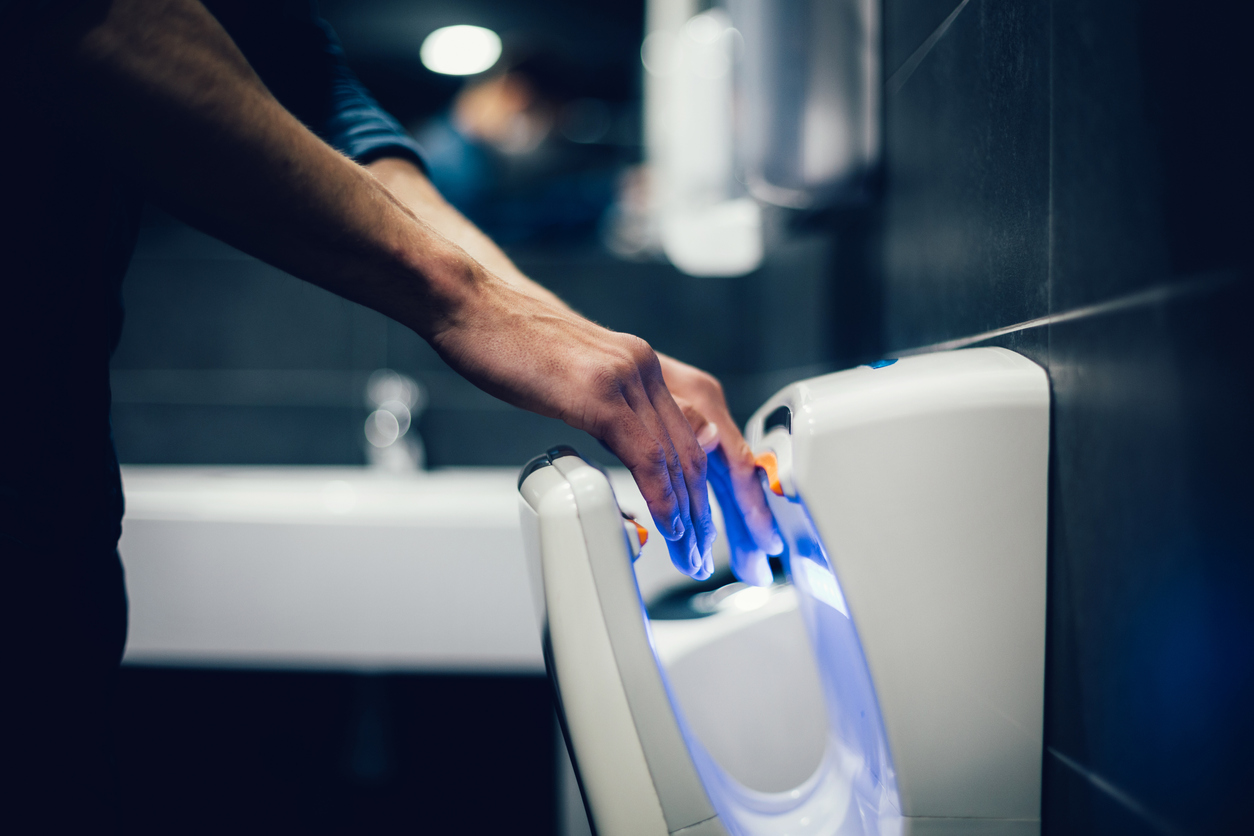 A man using a touch-free hand dryer in a bathroom after washing his hands