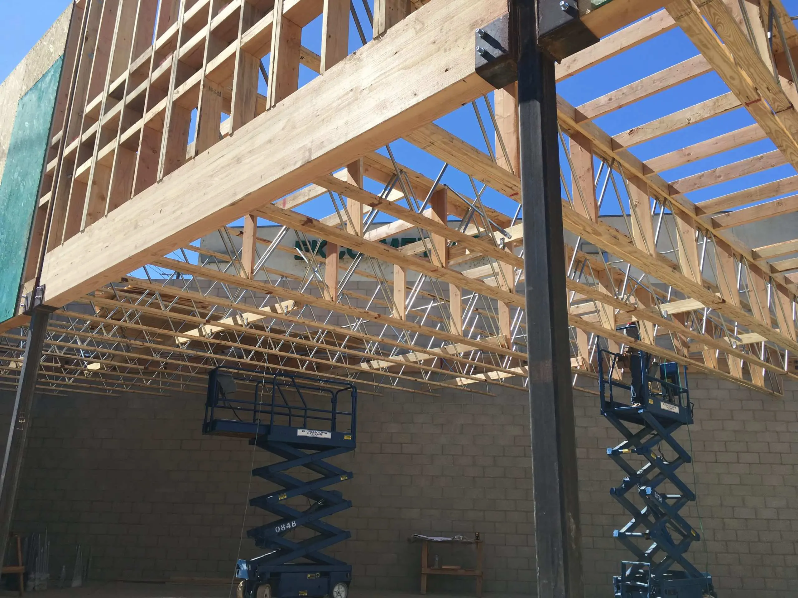 Two risen scissor lifts under a Los Angeles building's wooden roof frame