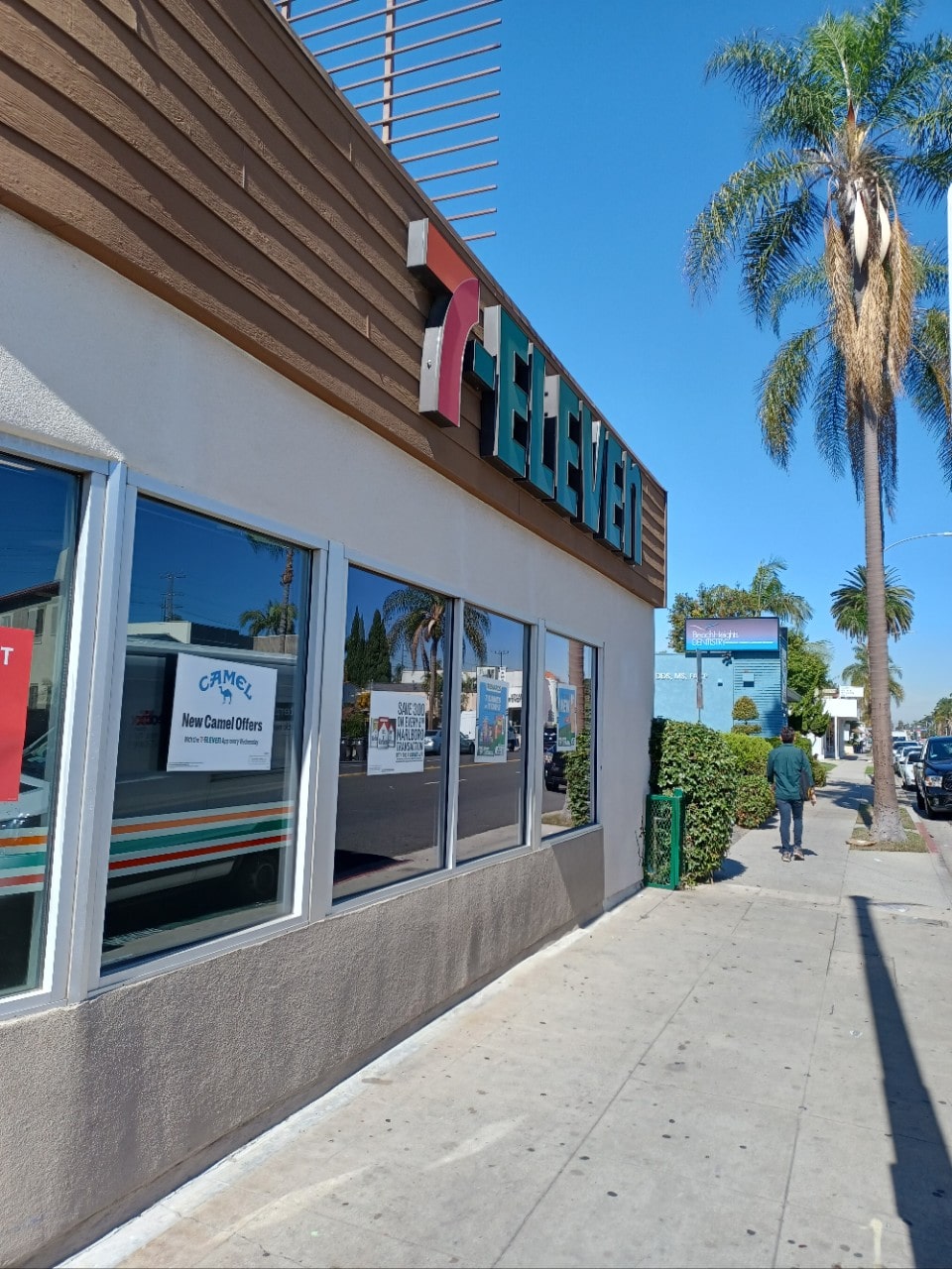 Exterior view of a 7-Eleven convenience store, displaying the iconic green and orange logo, with customers entering and exiting the store